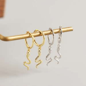 Detail of snake drop earrings in gold and silver finish with sparkling zircon eyes
