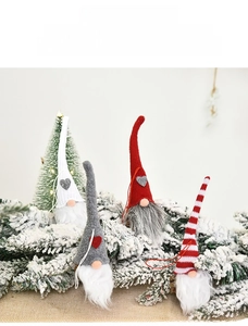 Detail of four handmade Christmas gnomes with knitted hats hanging on pine branches