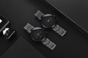 Detail view of two men's black steel watches with red and gold indices and calendar