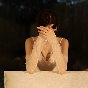 Detail of long bridal gloves in white mesh with pearl embellishments on model hands