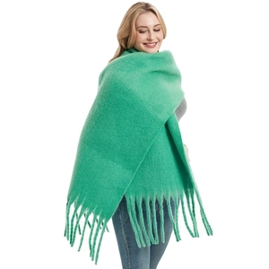 Detail view of large green knit scarf showing soft texture and long fringe tassels