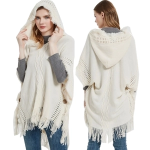 Detailed view of cream knitted hooded poncho featuring fringe trim and side buttons