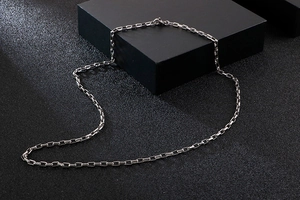 Detail shot of silver rectangular box chain necklace on elegant black textured background