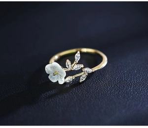 Detailed macro view of a gold flower ring with white petals and sparkling zircon leaf
