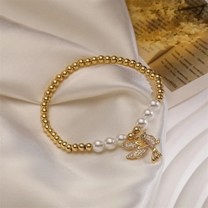 Detail of gold beads and white pearls bracelet with a sparkling bird charm on white silk