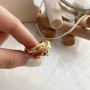 Primer plano de dos anillos de latón bañados en oro con circonitas sostenidos con la mano