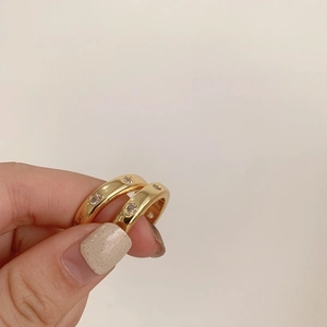 Detalle de dos anillos de latón chapado en oro con circonitas sobre un fondo de tono suave
