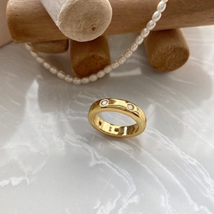 Detalle de anillo de latón bañado en oro con circonitas sobre superficie de mármol