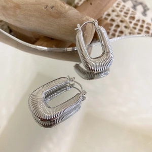 Macro detail of U-shaped silver woven metal earrings with ribbed texture on mirror surface