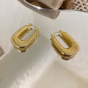 Detailed view of U-shaped woven gold hoop earrings with vertical ribbed texture and lever back