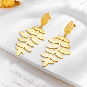 Elegant gold leaf dangle earrings with layered foliage design on a textured white surface