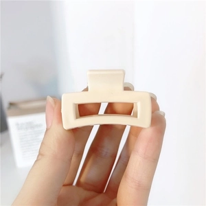 Close-up of minimalist cream square hair claw clip held by hand showing matte texture