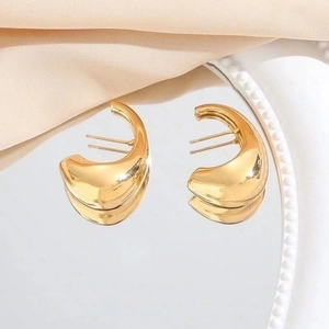Polished gold crescent moon hoop earrings on satin background with mirror reflection
