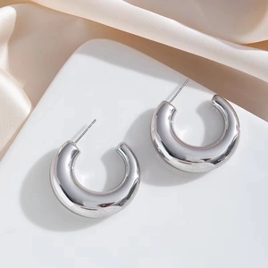 Polished silver C-shaped chunky hoop earrings on a minimalist white display stand