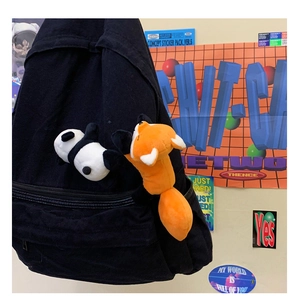 Detail of plush panda and orange fox charms attached to a black canvas backpack side