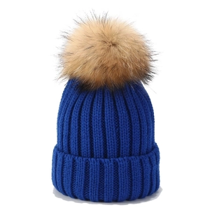 Detail der königsblauen Strickmütze mit flauschigem braunem Waschbär-Echtfellbommel