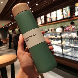Detailed view of a green mini 150ml vacuum bottle with wood grain cap held in hand