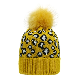Detail of yellow leopard print knit beanie featuring a large faux fur pompom and ribbed cuff