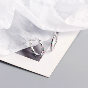Macro shot of silver hoop earrings with rainbow colored stones on white soft paper
