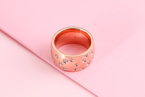 Detailed view of rose gold wide ring with sparkling pavé set diamonds on pink background