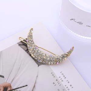 Detailed close-up of a crescent moon hair clip with sparkling rhinestones on golden metal