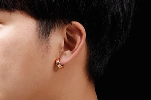 Détail d'une boucle d'oreille clip en or rose poli sur un fond noir contrasté