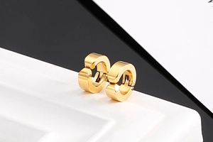 Détail de boucles d'oreilles clips dorées posées sur un socle blanc au design moderne
