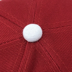 Close-up of a red twill baseball cap crown with a white fabric top button and stitching