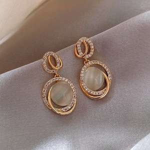 Makroaufnahme geometrischer Goldohrringe mit Katzenaugensteinen und glitzerndem Kristall-Pavé