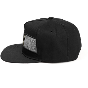 Détail de la casquette snapback noire avec écusson gris texturé et broderie jaune stylée