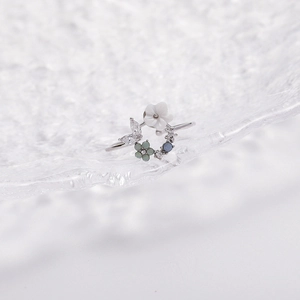 Detail of floral butterfly ring featuring white petals and blue stones on glass tray