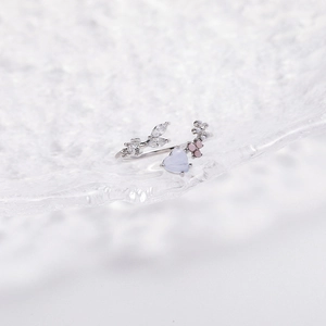Close-up of floral ring with blue heart stone and pink petals on glass surface