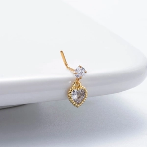 Detailed view of gold L-shaped nose stud with zircon heart pendant on white ceramic