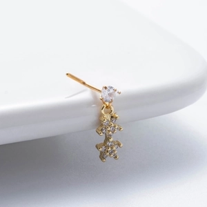 Macro detail of gold L-shaped nose stud with sparkling zircon flower pendant on ceramic