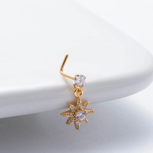 Macro shot of L-shaped gold nose stud with sparkling zircon starburst pendant detail