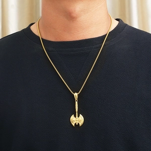 Close-up of a gold punk skull axe pendant with box chain worn by a male model
