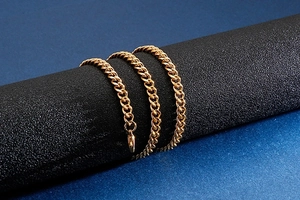 Detailed view of a golden curb chain necklace wrapped around a black matte prop