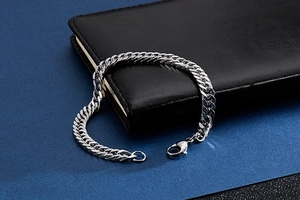 Close-up of a silver stainless steel Cuban link bracelet with a lobster clasp on leather