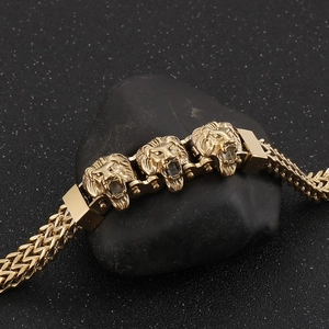 Detailed close-up of golden metal lion head charms on a double-loop braided chain bracelet
