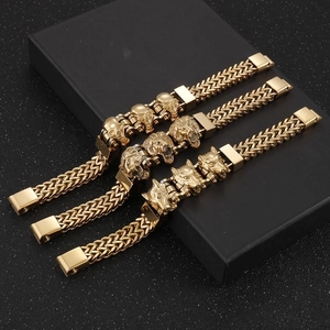 Three gold braided steel bracelets with skull, lion, and wolf heads on a gift box