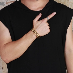 Detail of a men's gold lion head steel bracelet worn on wrist against a dark background
