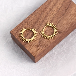 Detailed view of gold hoop earrings with sunburst bead texture on a dark wood block