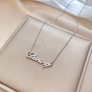 Macro shot of silver Darling pendant necklace on beige cushion with silk backdrop