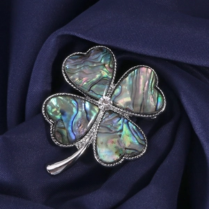 Macro shot of silver clover brooch with iridescent abalone shell on blue silk fabric