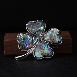 Macro shot of silver four-leaf clover brooch with iridescent shell inlay and crystal center