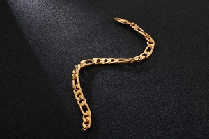 Macro shot of gold Figaro chain bracelet with polished links on black background