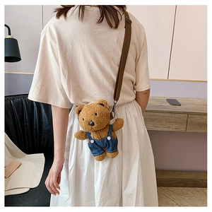 Brown plush bear crossbody bag with denim overalls shown on model in home setting
