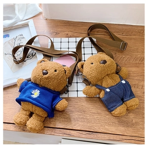 Detail of plush bear crossbody bags with floral tops and denim overalls on wood