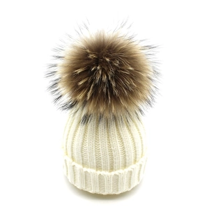 Detail of cream knit beanie with fluffy brown faux fur pom pom and warm ribbed texture