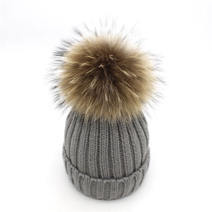 Detailed knit texture of dark grey winter hat with a fluffy brown faux fur pom pom